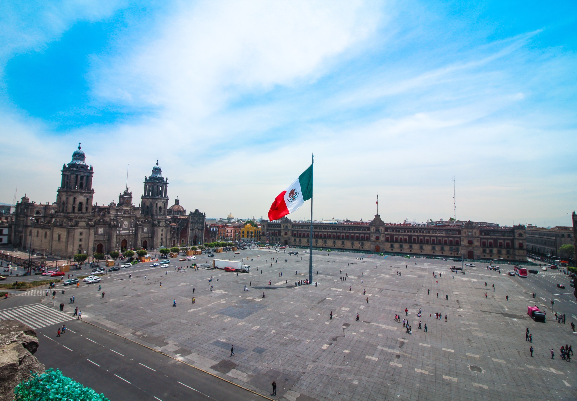 Mexican flag waving in Mexico’s centro histórico with cathedral and presidential palace in the back.